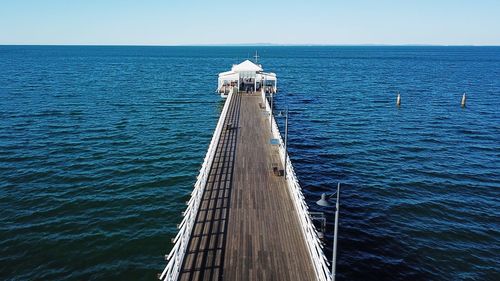 Pier over sea against clear blue sky
