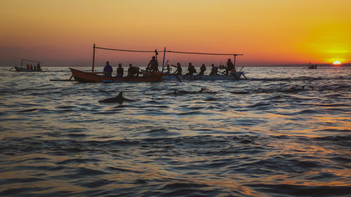 Silhouette people in sea against sky during sunset