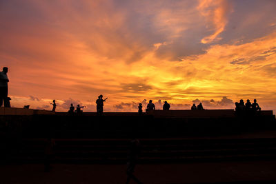 Silhouette people on beach against dramatic sky during sunset