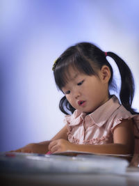Close-up of cute girl writing on book at table against wall