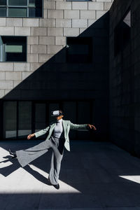 Businesswoman with virtual reality standing on one leg in front of office building