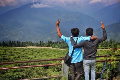 Rear view of men gesturing peace sign while looking at mountains