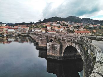 Arch bridge over river amidst buildings in city against sky