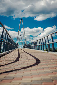 Empty footbridge against cloudy sky during sunny day