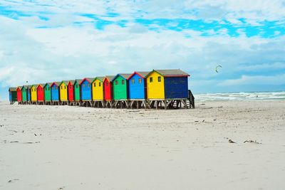 Multi colored huts on beach against cloudy sky