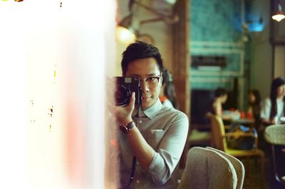 Young man photographing through camera while standing in restaurant