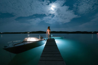 Rear view of woman standing on pier over sea against sky