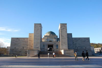 People walking in modern building against blue sky