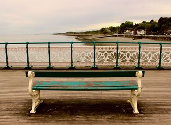 Empty bench on beach against sky