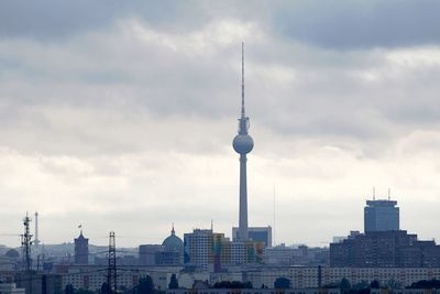 Communications tower in city against cloudy sky