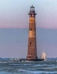 Old abandoned lighthouse by sea against sky with waves crashing against the base