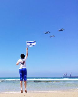 Rear view full length of boy holding israeli flag at beach