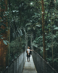 Woman standing on footbridge in forest