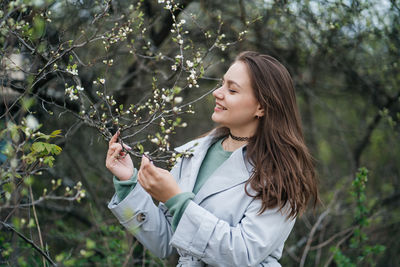 Beautiful girl with long hair in a grey trench coat outdoors in cherry blossoms in spring