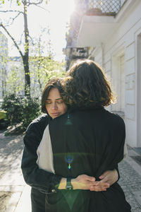 Lesbian couple embracing while standing on footpath during sunny day