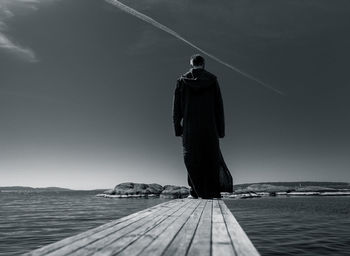 Rear view of man standing by sea on jetty