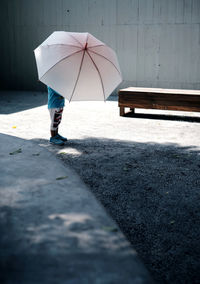 Low section of woman with umbrella walking on footpath