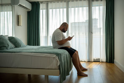 Side view of young woman sitting on bed at home