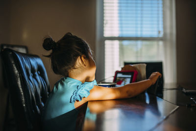 Side view of girl looking at video game while sitting at table