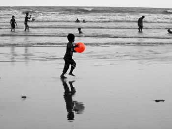 Boy playing with red ball while walking on sea shore