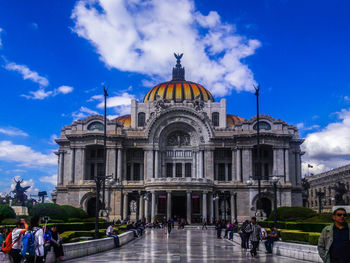 People in front of building against cloudy sky