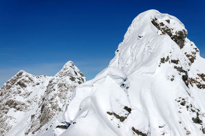 Low angle view of snow covered mountain against clear blue sky