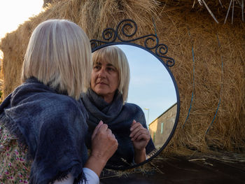 Reflection of woman in mirror by hay bales