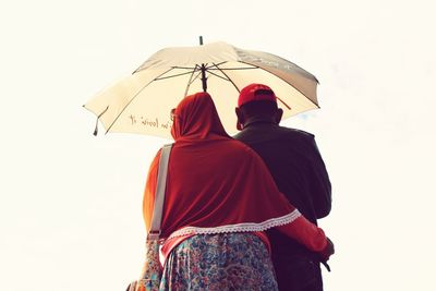 Rear view of couple holding umbrella against sky