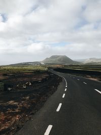 Road passing through landscape against cloudy sky