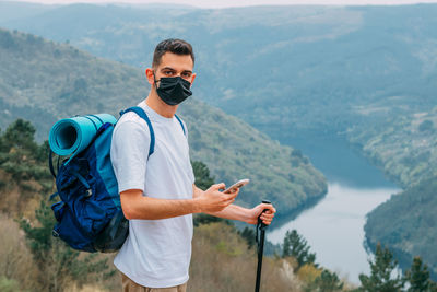 Young man protected with mask hiking in the mountains with mobile phone