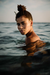 Portrait of shirtless young woman swimming in sea against sky