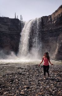 Full length of jumping woman standing against waterfall