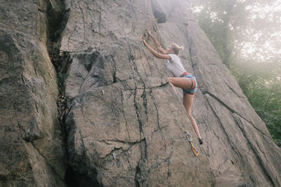 Low angle view of young woman climbing on rock formation