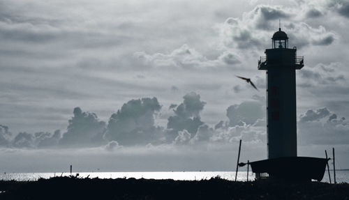 Silhouette lighthouse by sea against sky