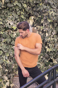 Muscular man posing next to a plant wall