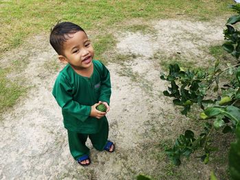 High angle view of cute boy holding fruit standing on field