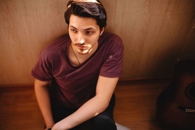 Thoughtful young man sitting on balcony floor at home