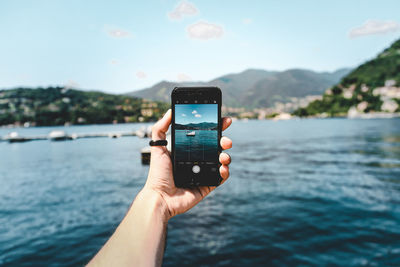 Close-up of hand holding mobile phone against river