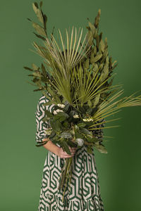 Young woman holding bunch of leaves against green background