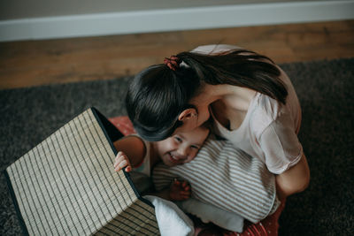  mother in a home suit is sitting at home on the floor, her daughter climbed into the laundry basket