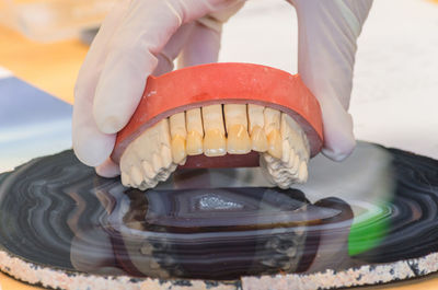 Cropped hand of person holding denture on table