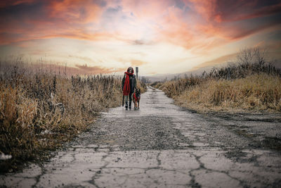 Rear view of man walking on road against sky during sunset