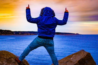 Rear view of man standing on rock by sea against sky