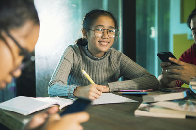 Portrait of smiling teenage girl studying while sitting with friends