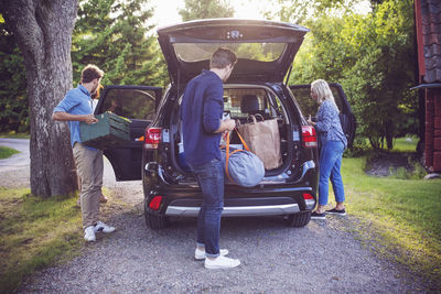 Friends loading luggage into car while standing on road