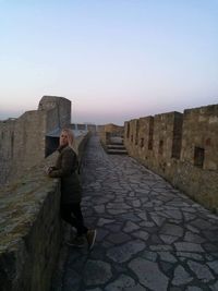 Man standing on stone wall against sky