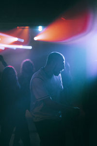 Cheerful young man dancing against illuminated spotlight at nightclub