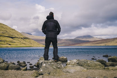 Rear view of man standing on rock against sky