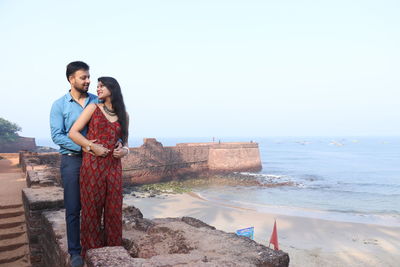 Couple standing on fort by beach against sea and sky