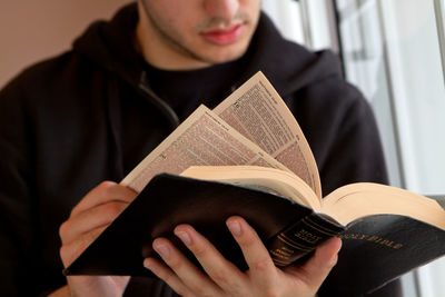 Midsection of young man reading bible at home 